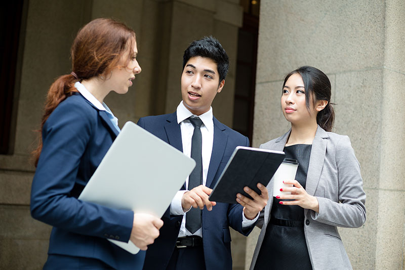 white female lawyer talking with a male and female asian lawyer outside in front of courthouse